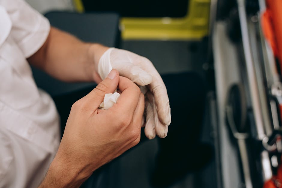 Close-up view of a person wearing a white shirt and white protective gloves, carefully handling a small object or detail during a house removal process. The background includes a partially visible black sofa or chair and some moving equipment, indicating an indoor setting in a home or property. The scene suggests attention to detail in packing or pre-move preparation, as part of a professional furniture transport or home relocation arranged by Man with Van Lamorbey, with packing materials and moving tools nearby to facilitate efficient loading and transportation of household items under the context of emergency same-day removals in Lamorbey.